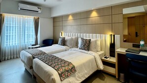 A hotel room with two beds, a desk, a chair, a ceiling fan, and a large window with curtains. - Galaxy Beacon Hotel (Mumbai)