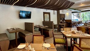 A restaurant with a modern interior, featuring a unique ceiling design, comfortable seating, and a large window providing a view of the outdoors. - Galaxy Beacon Hotel (Mumbai)