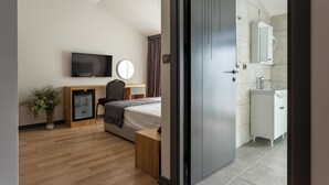 Une chambre d’hôtel moderne équipée d’un lit, d’une table de chevet, d’un bureau, d’une chaise, d’une télévision et d’une salle de bain avec un lavabo et un miroir.
