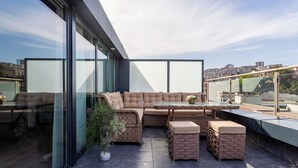 Un espace de détente extérieur moderne, comprenant un grand canapé d’angle, une table à plateau en verre et des poufs en osier.