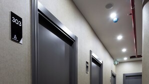 Un couloir avec des portes numérotées 303, 304 et 305, un sol recouvert de moquette et des spots encastrés au plafond.