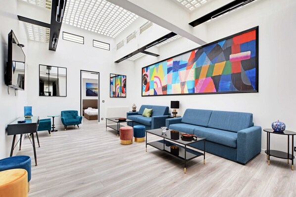 Un salon moderne avec un canapé bleu, une table basse et un grand tableau abstrait accroché au mur.