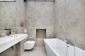 Une salle de bain moderne avec une grande baignoire, des toilettes et un meuble-lavabo avec un miroir.