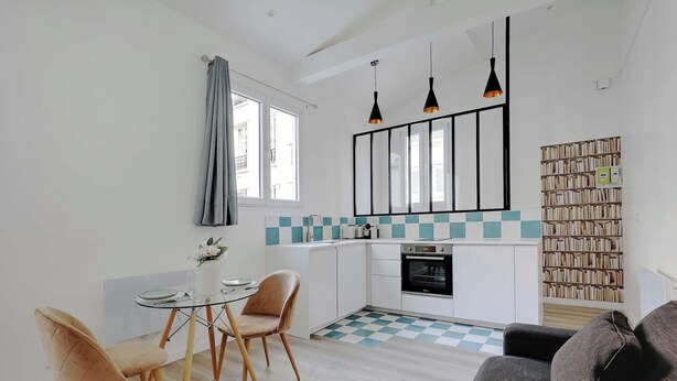 Une cuisine moderne avec un carrelage à motifs, un coin repas avec deux chaises, un canapé et une bibliothèque.