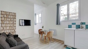 Un salon moderne comprenant un canapé, une table à manger avec des chaises, un téléviseur à écran plat fixé au mur et un coin cuisine avec un évier et des placards.