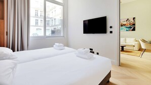 A hotel room with two beds, a TV mounted on the wall, and a view of the city through the window.
