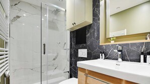 A modern bathroom with a glass-enclosed shower, a white toilet, and a vanity with a marble backsplash. - Welcoming apartment -1BD/4P - 18th arrd (Paris)