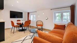 A modern living room with a sofa, dining table, chairs, and a TV mounted on the wall. - Welcoming apartment -1BD/4P - 18th arrd (Paris)