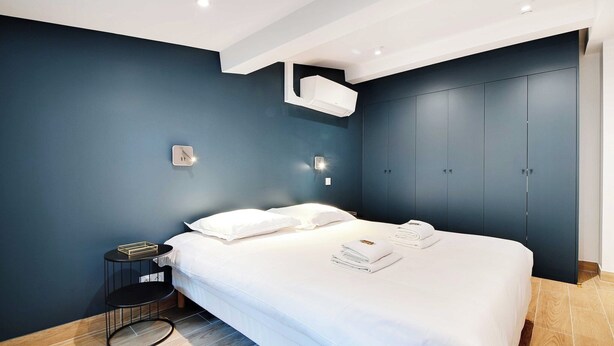 A modern bedroom with a large bed, dark blue walls, and a built-in wardrobe. - Welcoming apartment -1BD/4P - 18th arrd (Paris)
