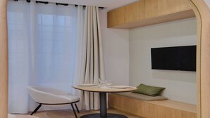 A modern room with a round table, a chair, a sofa, a TV, and a window with curtains. - Modern studio - 2P - Clignancourt (Paris)