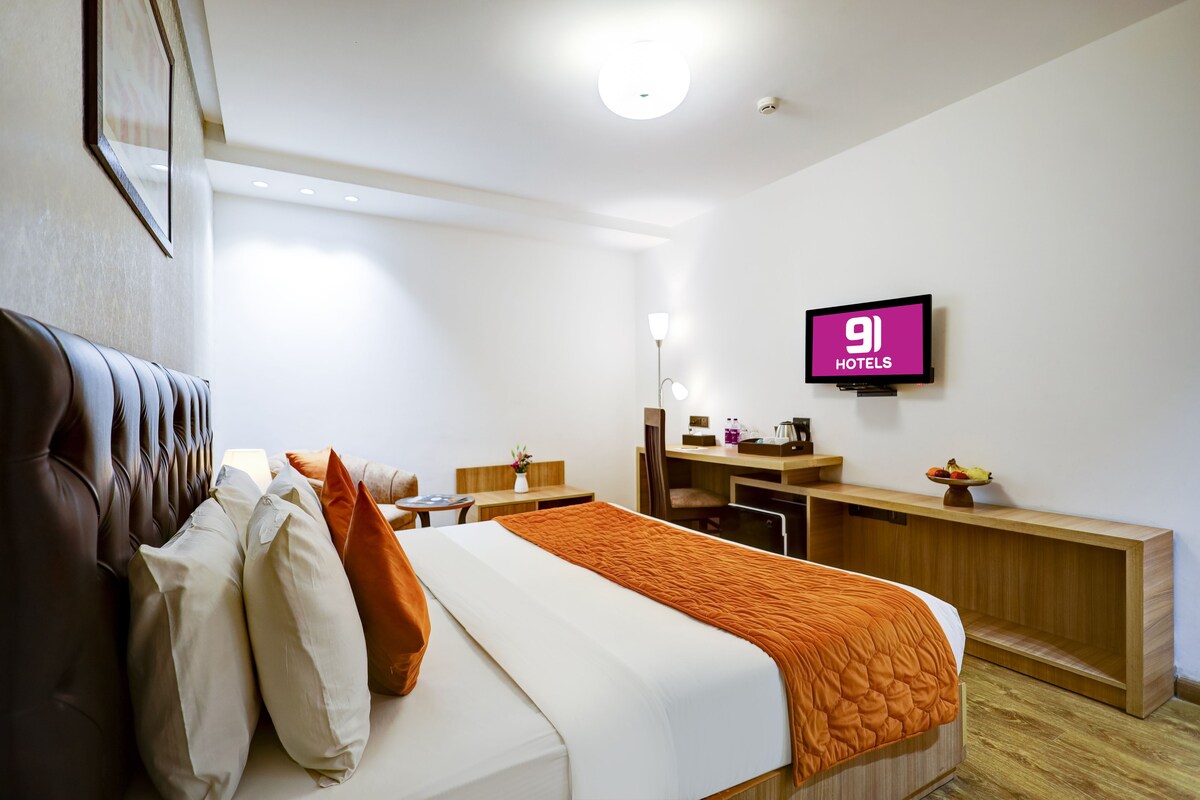 Ein Hotelzimmer mit einem Bett, einem Schreibtisch, einem Sessel, einem Fernseher und einem kleinen Tisch mit einer Vase.