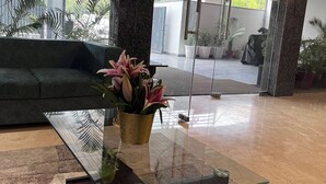 A modern lobby with a glass coffee table, a green sofa, and potted plants. - Hotel 91 Huda City Centre (Gurugram)