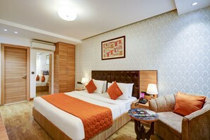 Een hotelkamer met een groot bed, een slaapbank, een klein tafeltje en een kunstwerk aan de muur.