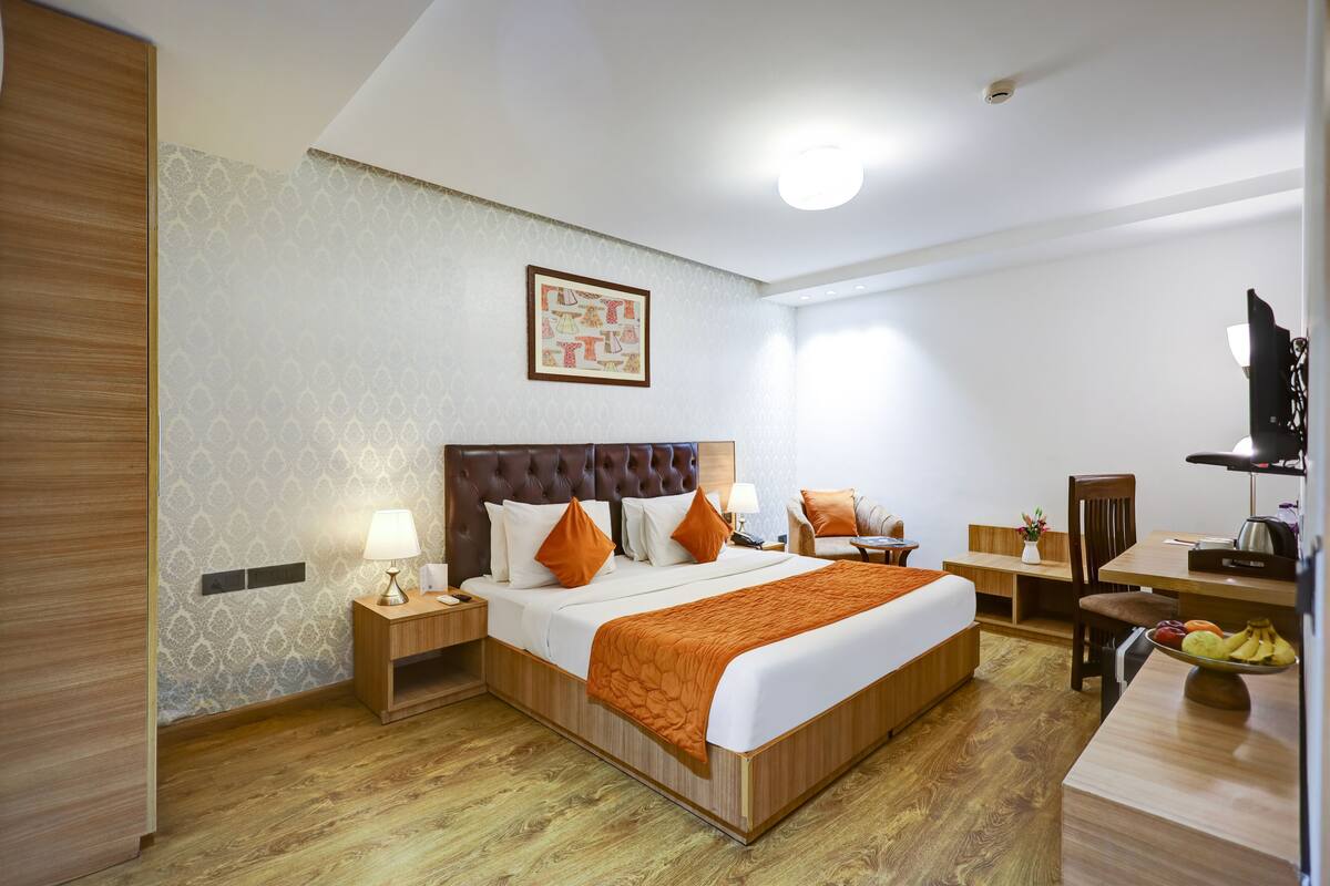 Hotelkamer met een groot bed, houten hoofdeinde, twee nachtkastjes met lampen, een bureau met stoel, en een fruitschaal op het bureau.