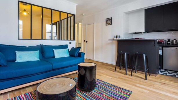 A modern living room with a blue sofa, a coffee table, and a large window with a view. - Cosy apartment - 4P - Place de la Bastille (Paris)