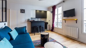 A modern apartment with a blue sofa, a kitchen area, and a TV mounted on the wall. - Cosy apartment - 4P - Place de la Bastille (Paris)