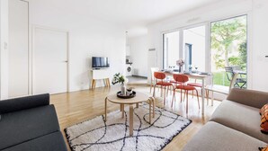 Una sala moderna con un sofá, una zona de comedor con sillas, un televisor y una cocina al fondo.