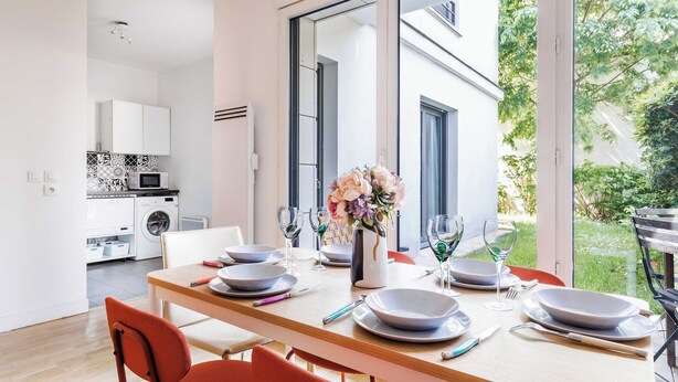 Comedor con una mesa lista para cuatro, cocina al fondo y vista a zonas verdes al exterior.