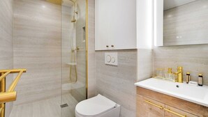 Une salle de bain moderne avec une douche à parois de verre, des toilettes blanches et un meuble-lavabo avec des accessoires dorés.