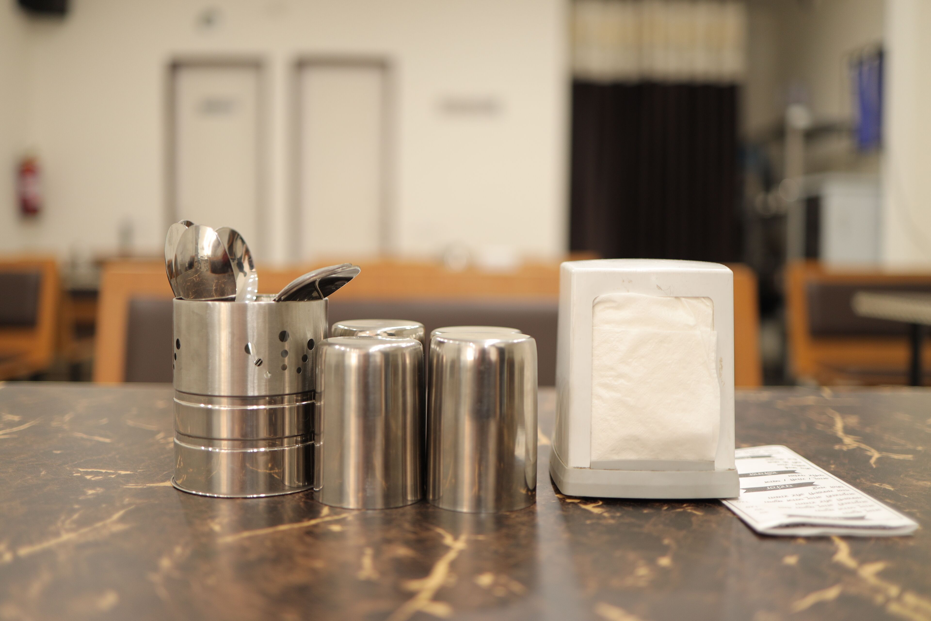 A table with a salt and pepper shaker set, a white napkin dispenser, and a menu on a marble surface in a hotel lobby.