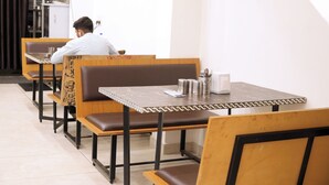 A restaurant with wooden booths and tables, a person seated at a booth, and a staircase leading to an upper level. - Atithi Hotel and Dhaba (Panipat)