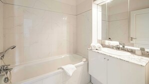 Ein modernes Badezimmer mit einer Marmorwand, einer freistehenden Badewanne, einem Waschbecken mit Marmorplatte und einem großen Spiegel darüber.