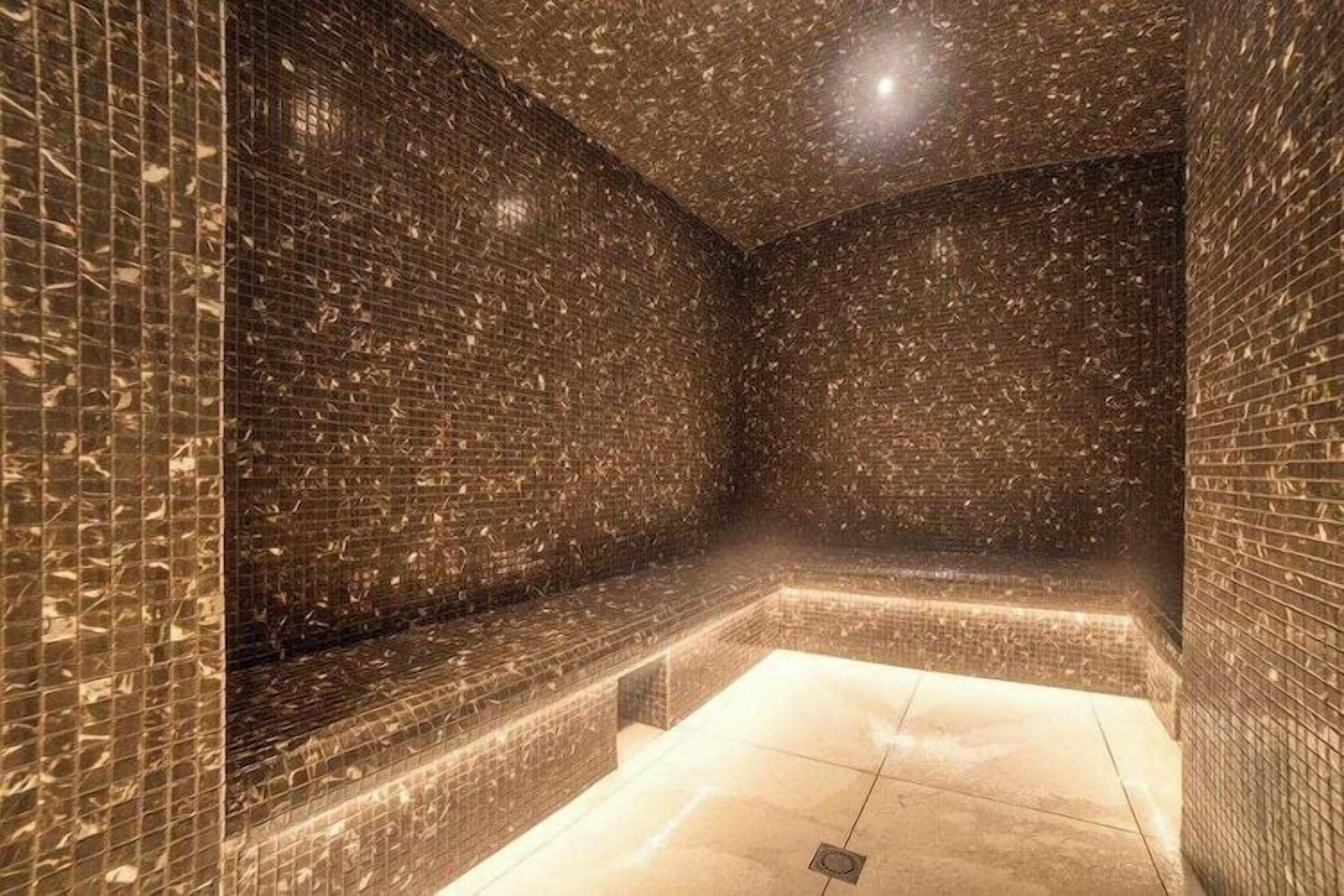 Un cuarto de spa con piso y paredes de azulejos, un banco y una lámpara en el techo.