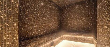 Un cuarto de spa con piso y paredes de azulejos, un banco y una lámpara en el techo.
