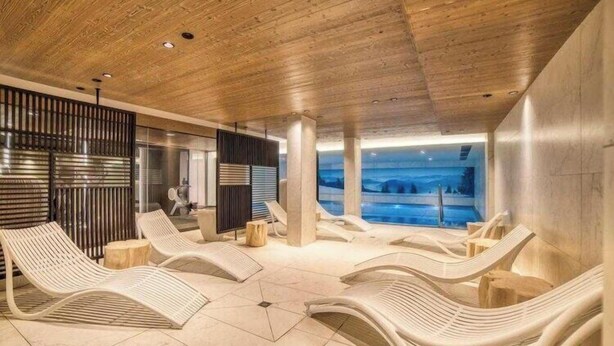 A modern indoor pool area with lounge chairs and a view of the outdoors. - Luxurious 4-room apartment with swimming pool, gym, spa and parking (Megève)