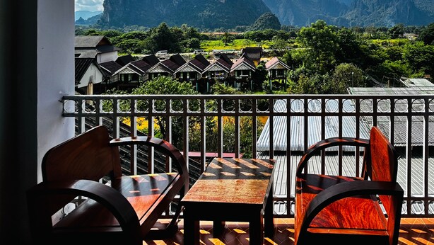 A balcony with a view of traditional houses and mountains. - Domon Riverside Hotel (Vang Vieng)