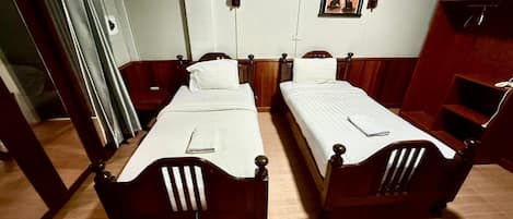 A room with two wooden beds, a small table, and a wall-mounted picture.