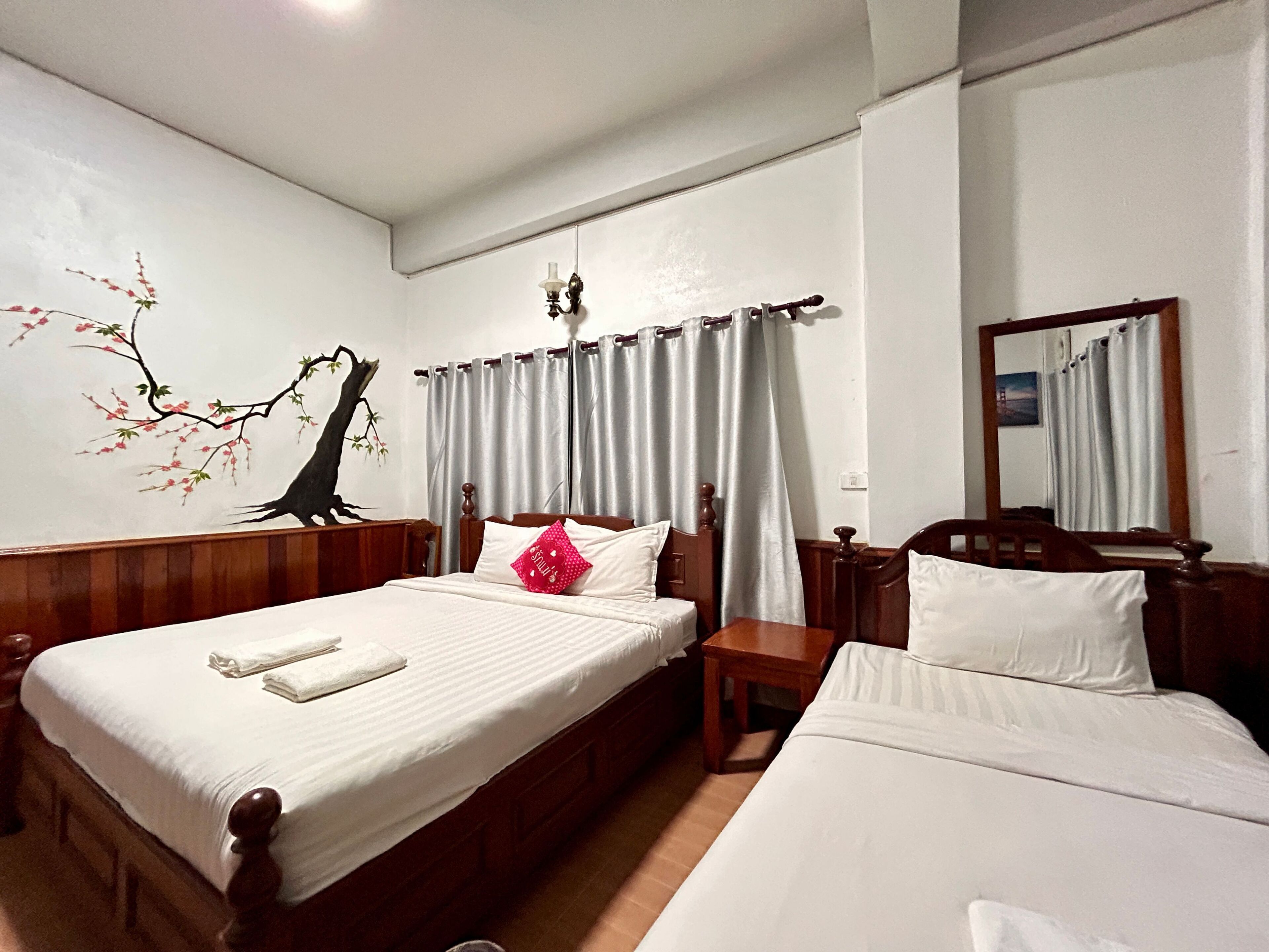 A hotel room with two beds, a wooden headboard, a wall-mounted lamp, and a large mirror.