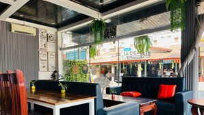 A modern cafe with a wooden table, black and blue seating, and green plants. - Domon Riverside Hotel (Vang Vieng)