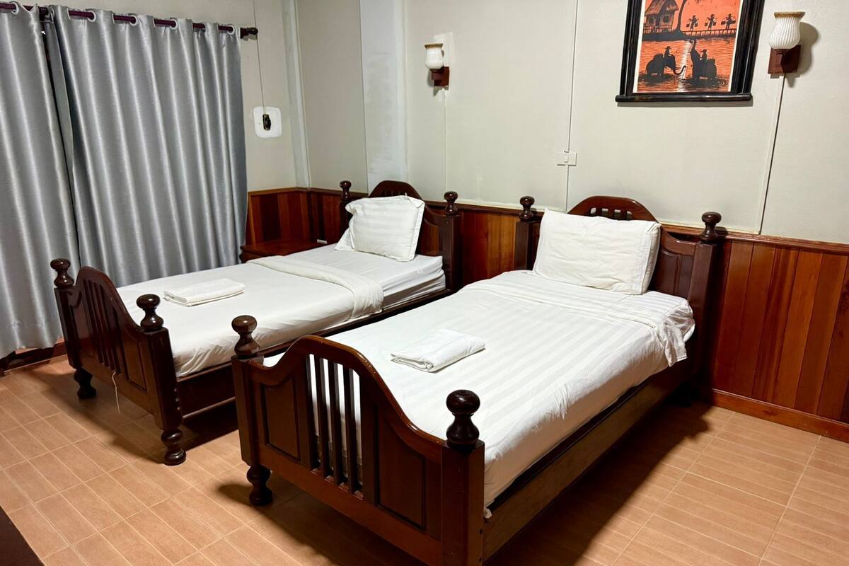 A room with two wooden beds, a curtain, a wall-mounted light, and a framed picture.