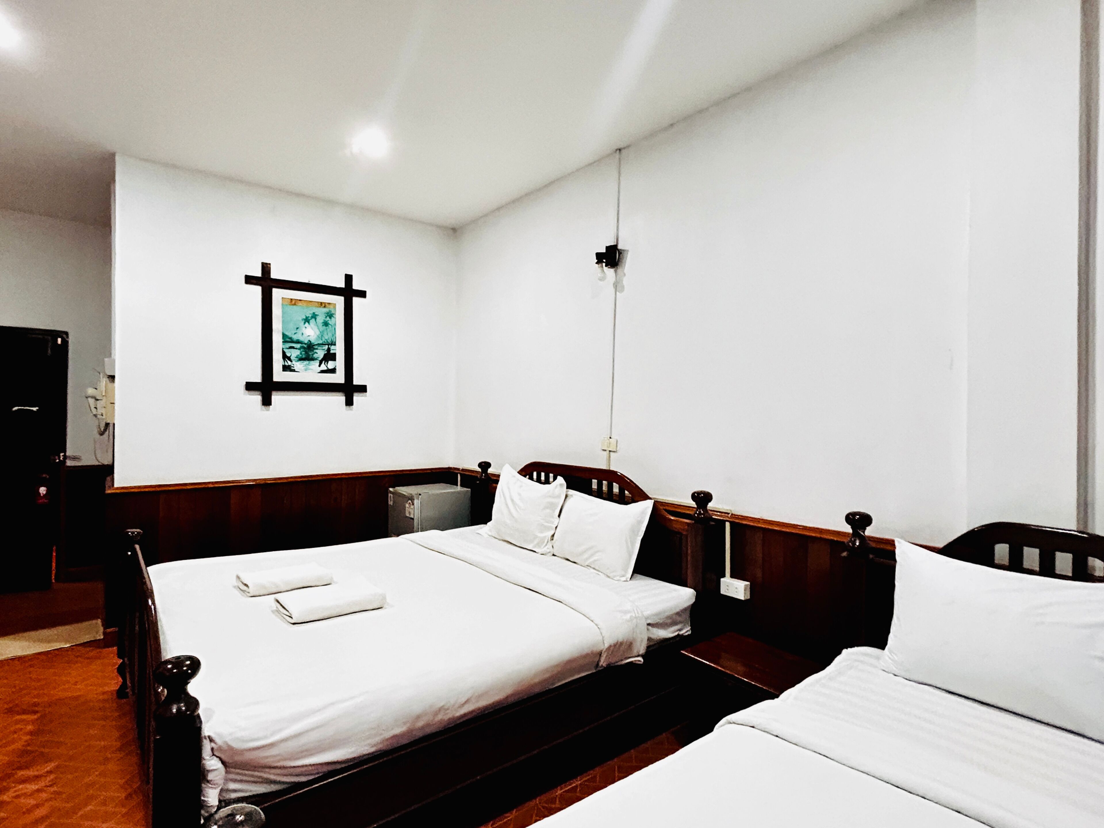 Ein Hotelzimmer mit zwei Einzelbetten, einem Holzkopfende, einem kleinen Nachttisch und einem an der Wand hängenden Bild.