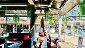 An indoor seating area with a sofa, chairs, and a table, featuring a view of the street outside. - Domon Riverside Hotel (Vang Vieng)