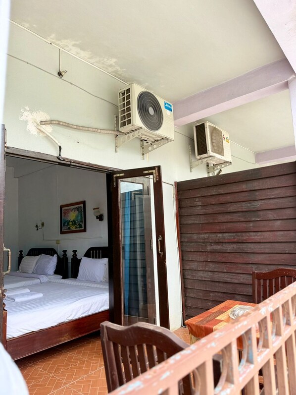 A room with two beds, a wooden table, and an air conditioning unit mounted on the wall.