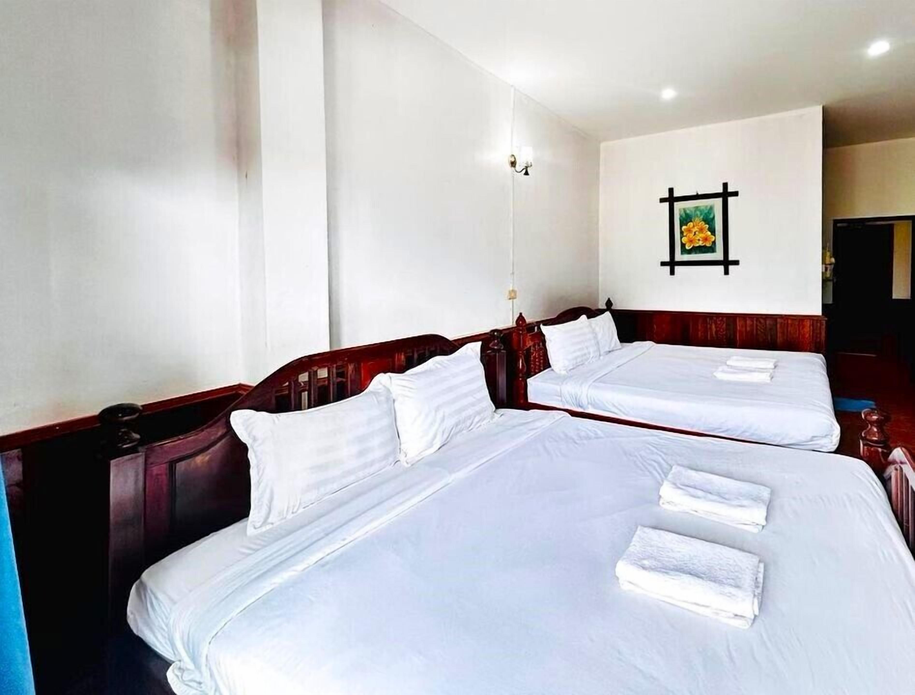 Habitación de hotel con dos camas, ropa de cama blanca, cabecero de madera, un cuadro colgado en la pared y una lámpara de noche.