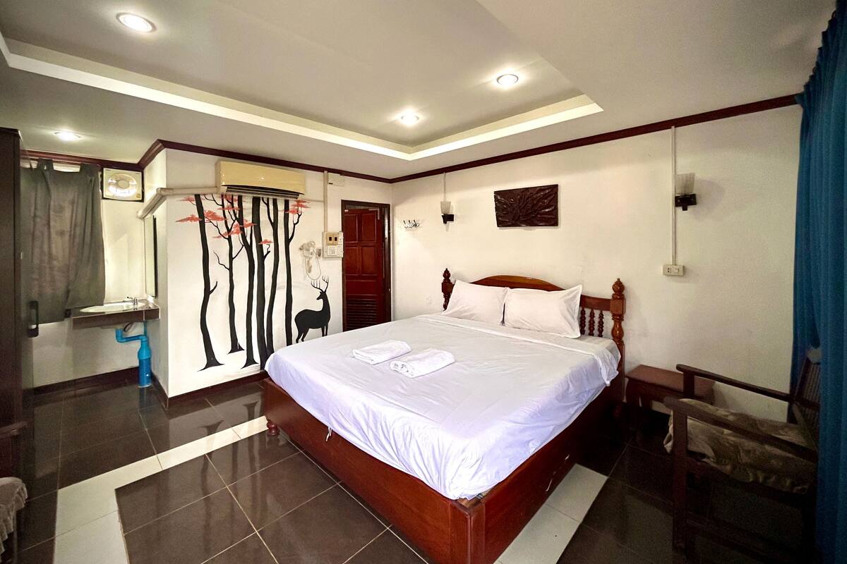 A bedroom with a large bed, a bedside table, a mirror, and a wall-mounted air conditioning unit.