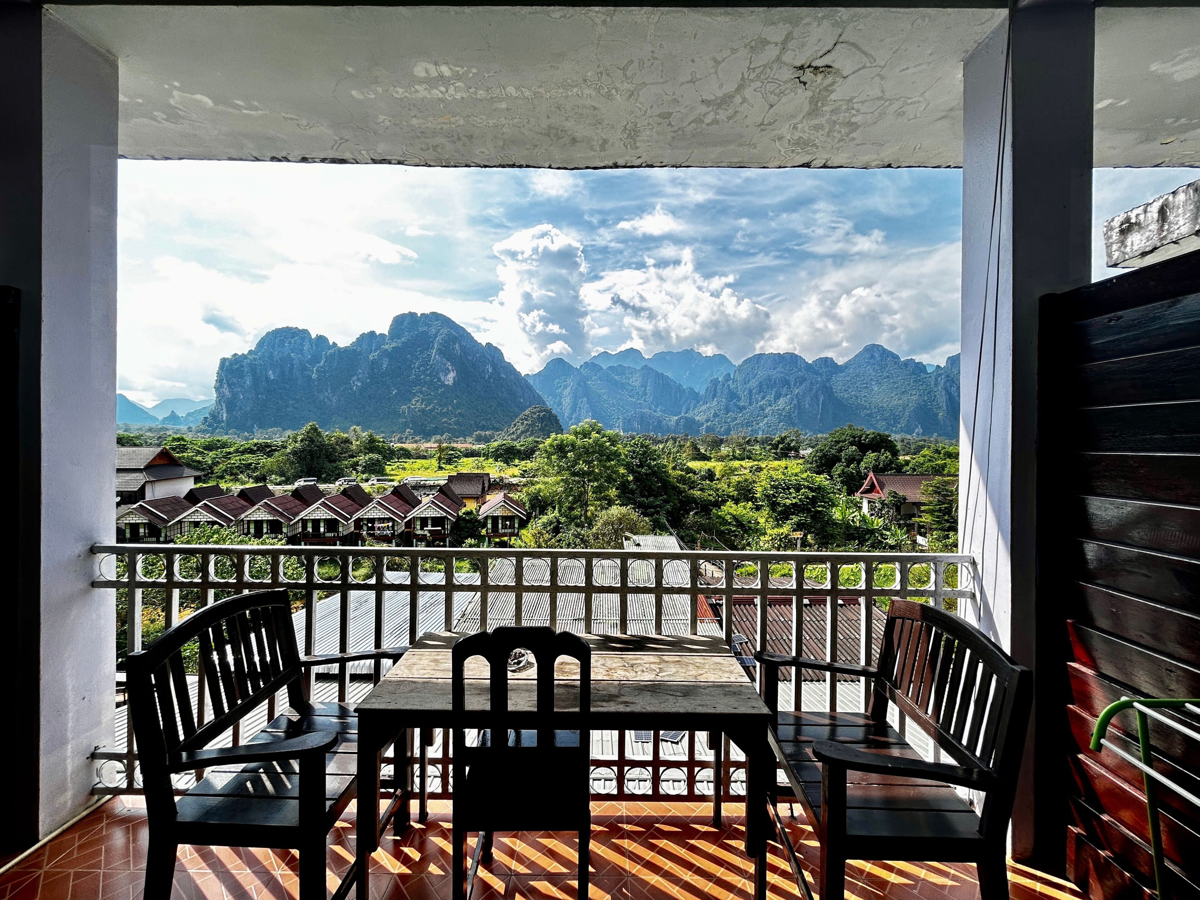 Un balcon avec une table et des chaises, donnant sur un paysage montagneux avec des bâtiments visibles au loin.