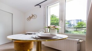 A modern dining area with a round table, gold accents, and a view of greenery and buildings through a large window. - Superb studio - 2P - Beaugrenelle / Tour Eiffel (Paris)