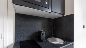 A kitchen with a black countertop, a sink, a coffee machine, and a microwave. - Superb studio - 2P - Beaugrenelle / Tour Eiffel (Paris)