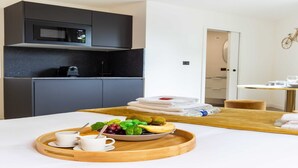 A modern hotel room with a kitchen area, a dining table with a tray of food, and a neatly made bed. - Superb studio - 2P - Beaugrenelle / Tour Eiffel (Paris)
