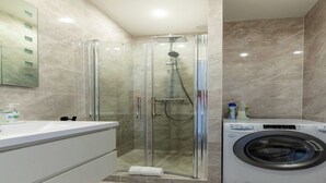 A modern bathroom with a glass-enclosed shower, a built-in washing machine, and a large mirror.