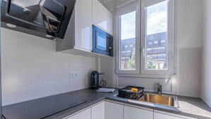 A modern kitchen with white cabinets, a black countertop, a microwave, a kettle, and a sink.