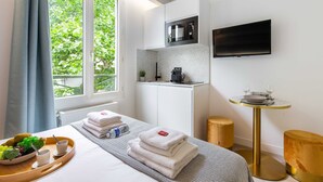A modern hotel room with a bed, a breakfast tray, a small kitchen area, a TV, and a window with a view of greenery. - Cosy Studio - Beaugrenelle parc des expositions 4 (Paris)