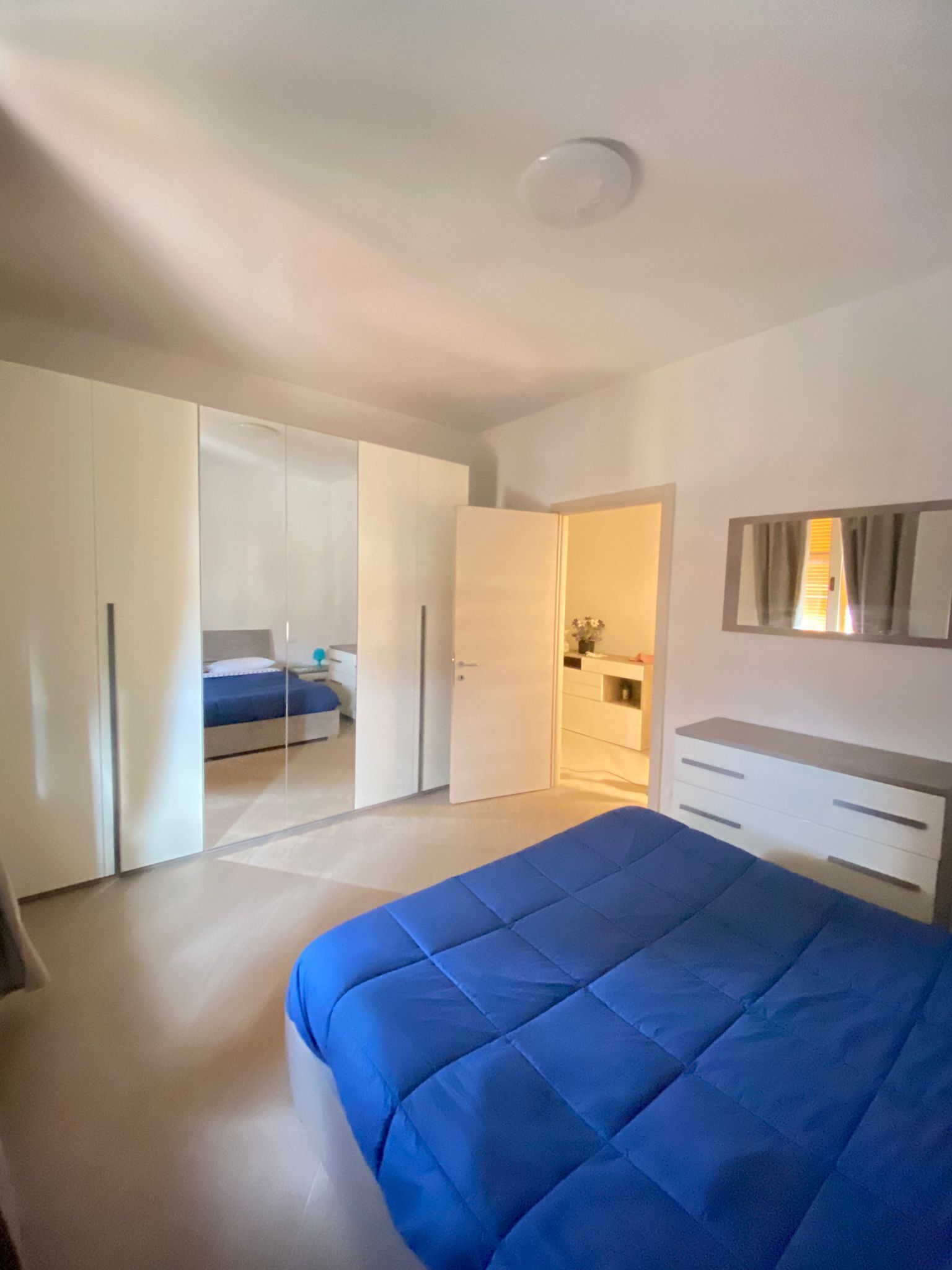 Een slaapkamer met een groot bed, een kledingkast, een spiegel en een klein badgedeelte.