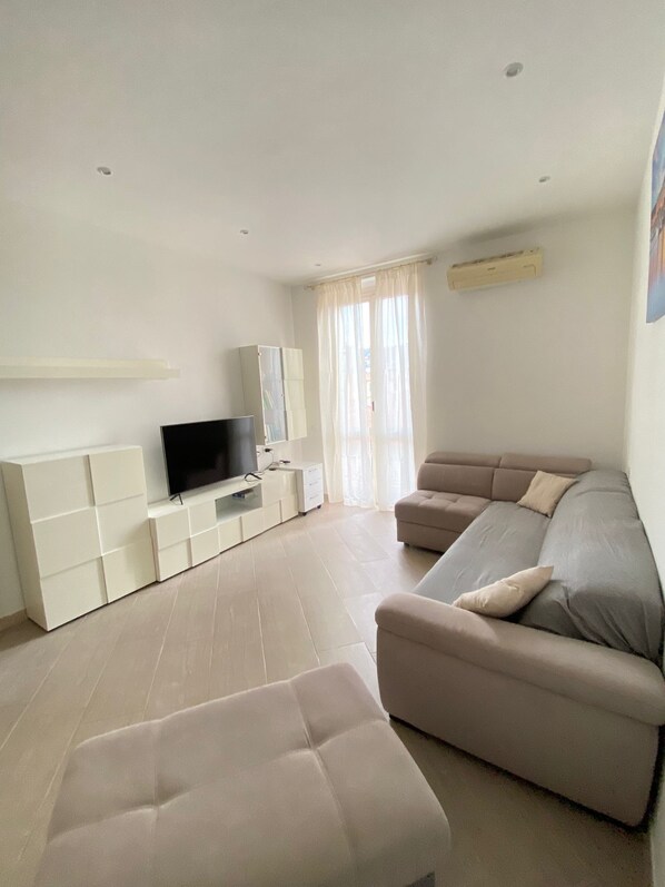 A modern living room with a sectional sofa, a flat-screen TV, and a built-in entertainment unit. - Casa Vacanza Le Cinque Terre (La Spezia)