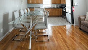 A modern kitchen with wooden cabinets, a glass dining table, and a stainless steel refrigerator. - Newark Liberty Gem Brick House - Apt 3 (Newark)
