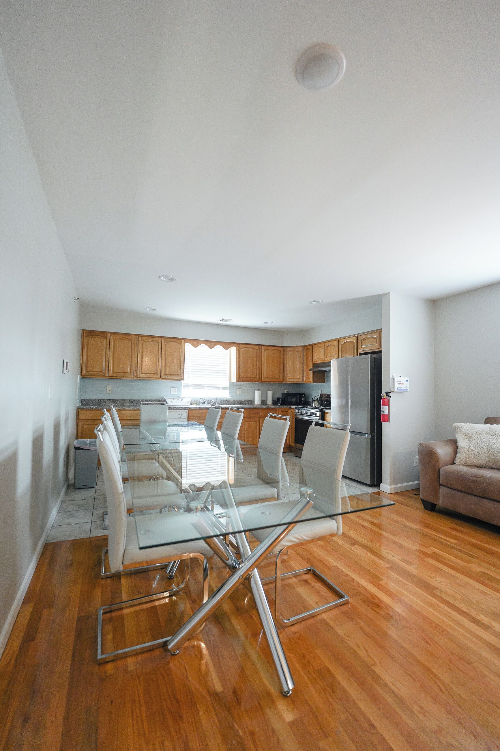 A modern kitchen with wooden cabinets, a stainless steel refrigerator, and a glass dining table with chairs.